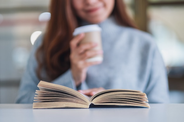 Immagine del primo piano di una donna che legge un libro mentre beve caffè su un tavolo di legno