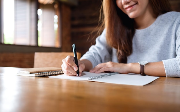 Immagine del primo piano di una donna che scrive su un taccuino bianco su un tavolo di legno