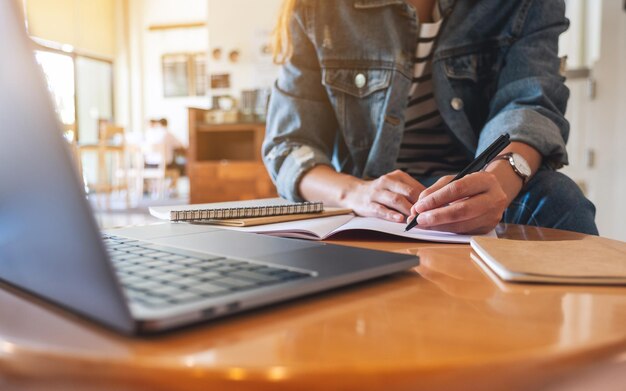 Immagine del primo piano di una donna che scrive su un taccuino con il computer portatile sul tavolo