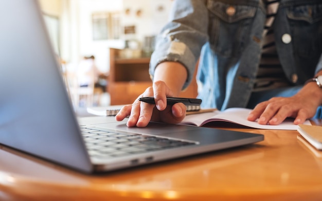 Immagine del primo piano di una donna che scrive su un taccuino mentre lavora al computer portatile in ufficio