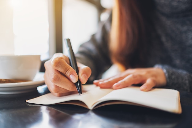 Immagine del primo piano di una donna che scrive su un taccuino vuoto sul tavolo