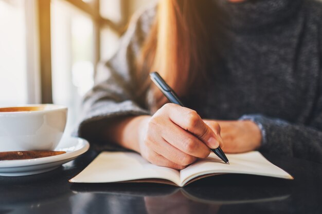 Immagine del primo piano di una donna che scrive su un taccuino vuoto sul tavolo