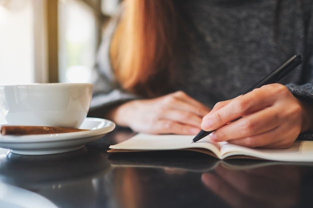 Immagine del primo piano di una donna che scrive su un taccuino vuoto sul tavolo