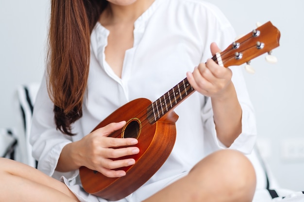 Immagine del primo piano di una donna che si siede e che gioca ukulele in camera da letto