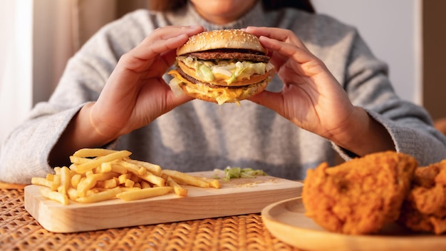 Immagine del primo piano di una donna che tiene e mangia hamburger e patatine fritte con pollo fritto sul tavolo a casa