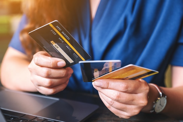 Immagine del primo piano di una donna che tiene e sceglie le carte di credito mentre usa il computer portatile