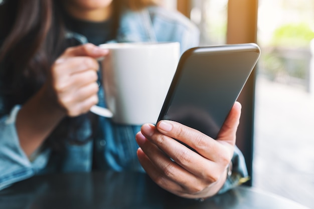 Immagine del primo piano di una donna che tiene e usa il telefono cellulare mentre beve caffè