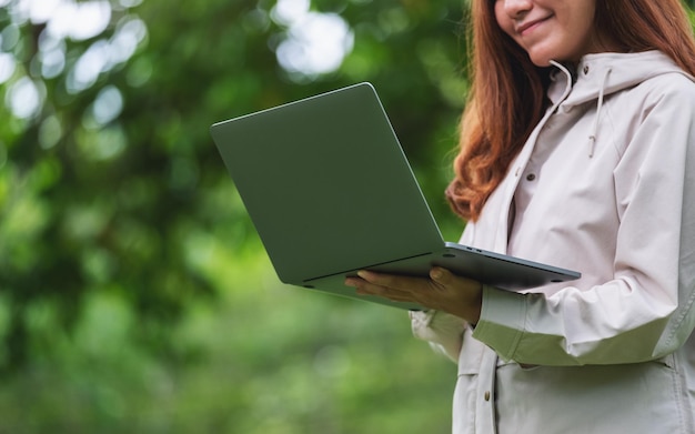 Immagine del primo piano di una donna che tiene e utilizza il computer portatile in mezzo alla natura