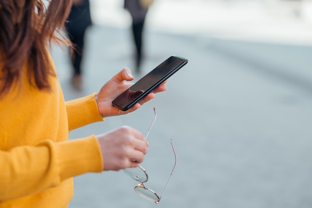 Immagine del primo piano di una donna che tiene gli occhiali e che utilizza Smart Phone nella via della città.