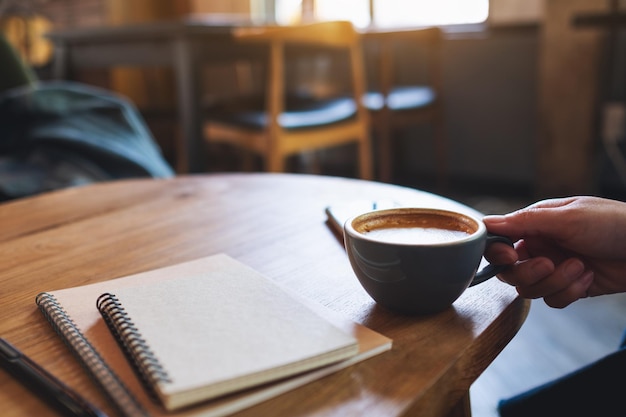 Immagine del primo piano di una donna che tiene la tazza di caffè con i taccuini sulla tavola di legno