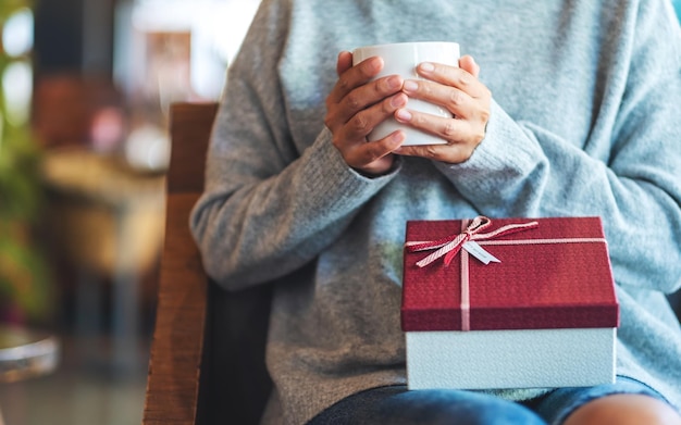 Immagine del primo piano di una donna che tiene un contenitore di regalo mentre beve il caffè