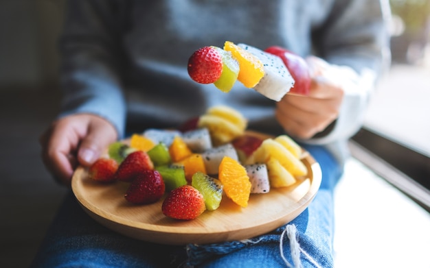 Immagine del primo piano di una donna che tiene un piatto di legno di frutta fresca mista su spiedini