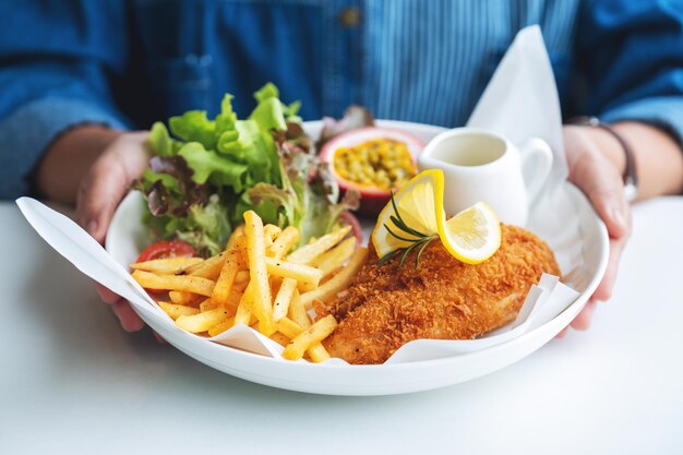 Immagine del primo piano di una donna che tiene un piatto di pesce e patatine fritte sul tavolo del ristorante