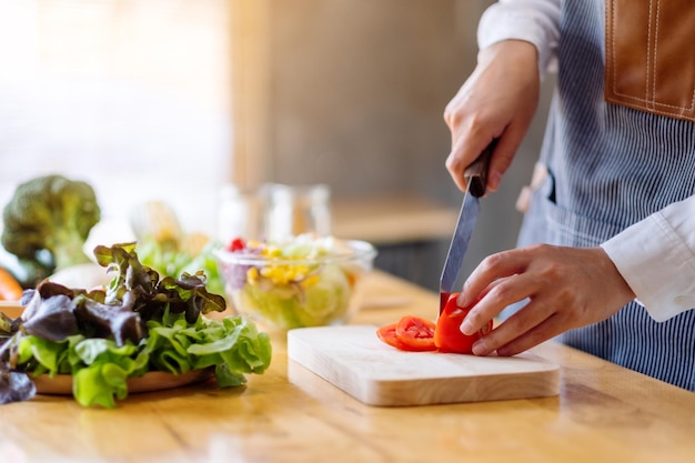 Immagine del primo piano di una donna chef che taglia e trita il pomodoro con un coltello su una tavola di legno