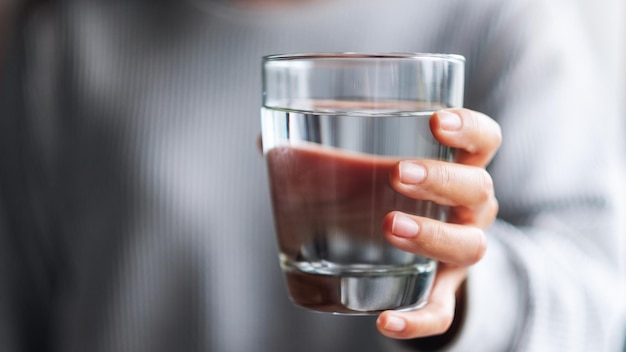 Immagine del primo piano di una donna con in mano un bicchiere di acqua pura