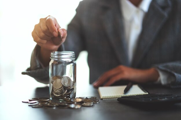 Immagine del primo piano di una donna d'affari che raccoglie e mette monete in un barattolo di vetro per risparmiare denaro concetto