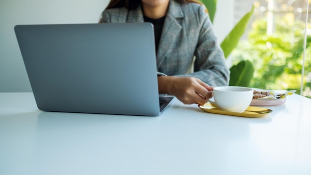 Immagine del primo piano di una donna d'affari che utilizza e lavora al computer portatile mentre beve caffè in ufficio