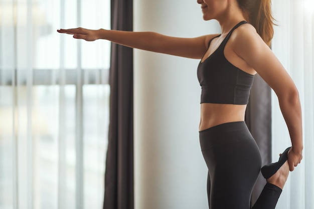 Immagine del primo piano di una donna fitness che allunga la gamba e il braccio mentre si riscalda prima dell'allenamento a casa