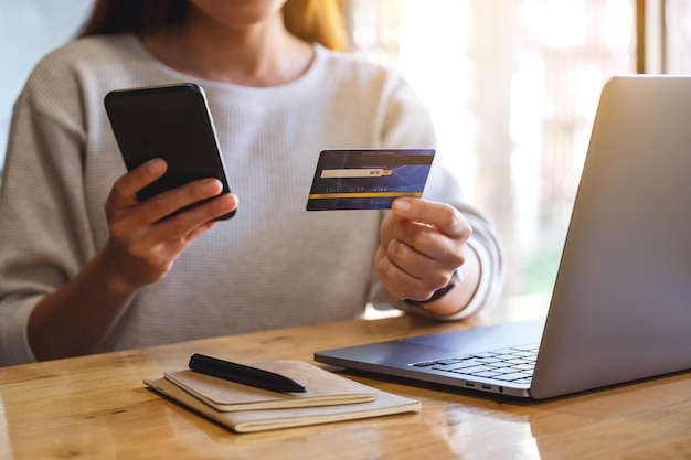 Immagine del primo piano di una donna in possesso di carta di credito durante l'utilizzo di smartphone e laptop in ufficio
