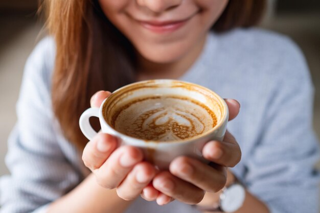 Immagine del primo piano di una giovane donna asiatica che tiene e che beve caffè caldo