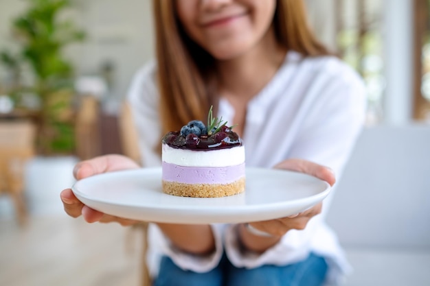 Immagine del primo piano di una giovane donna asiatica che tiene e mostra un piatto di cheesecake ai mirtilli