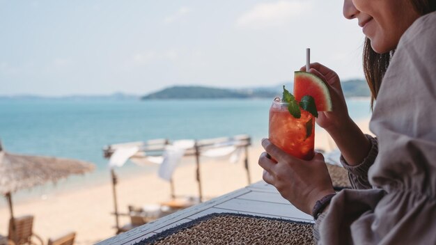 Immagine del primo piano di una giovane donna che beve succo di anguria mentre è seduto nel bar sulla spiaggia