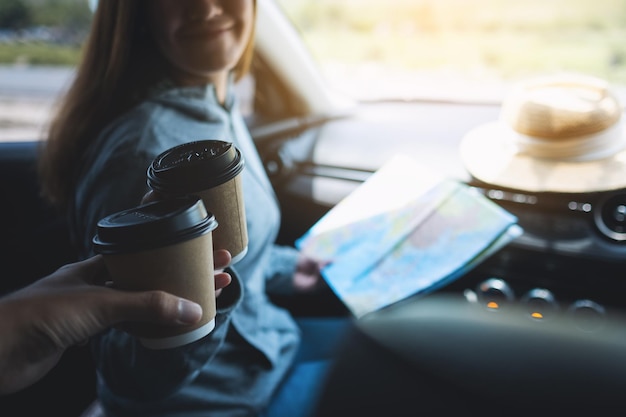 Immagine del primo piano di una giovane donna che fa tintinnare la tazza di caffè con un amico mentre si guida in macchina