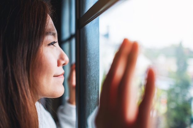 Immagine del primo piano di una giovane donna che tocca la finestra mentre guarda fuori