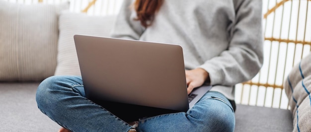 Immagine del primo piano di una giovane donna che utilizza e lavora al computer portatile mentre è seduta su un divano a casa