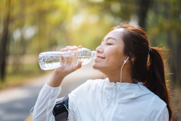 Immagine del primo piano di una runner asiatica che beve acqua dalla bottiglia dopo aver fatto jogging nel parco cittadino