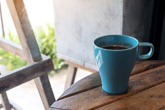 Immagine del primo piano di una tazza blu di caffè caldo sulla tavola di legno dell&#39;annata in caffè