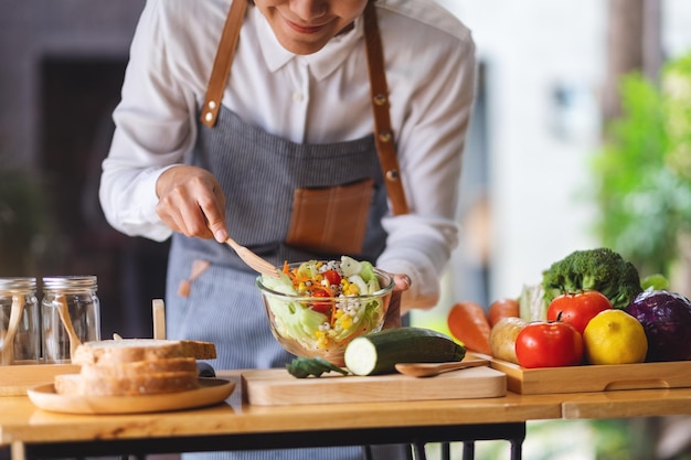 Immagine del primo piano di uno chef femminile che cucina insalata di verdure miste fresche in cucina