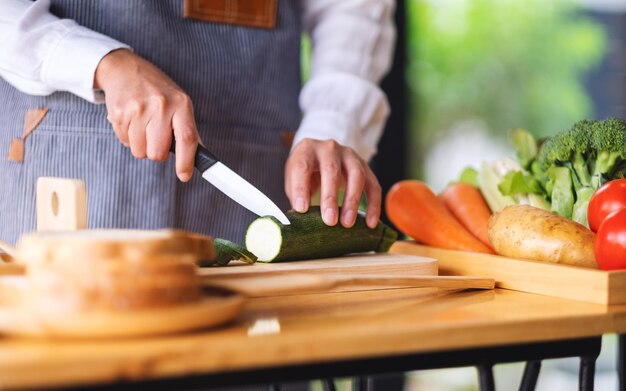 Immagine del primo piano di uno chef femminile che taglia e trita le verdure con un coltello su una tavola di legno in cucina