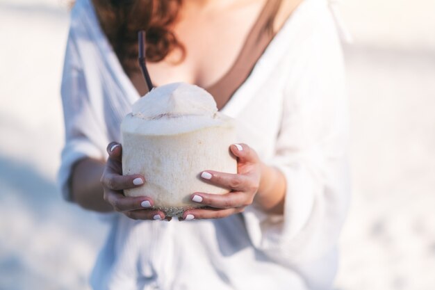 Immagine del primo piano una bella donna asiatica che tiene e beve succo di cocco sulla spiaggia