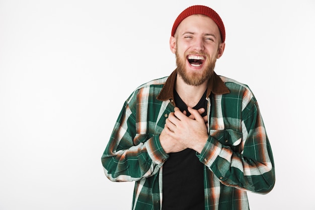 Immagine del ragazzo barbuto felice che indossa un cappello e camicia a quadri ridendo, mentre in piedi isolato su sfondo bianco