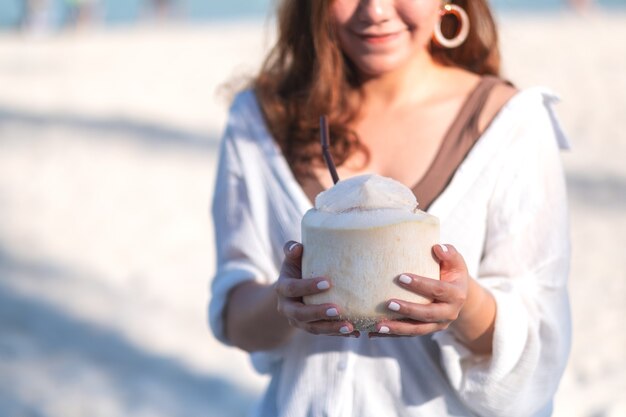 Immagine del ritratto di bella donna asiatica che tiene e che beve il succo di cocco sulla spiaggia