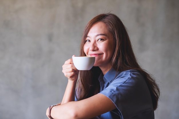 Immagine del ritratto di bella giovane donna asiatica che tiene e che beve caffè caldo