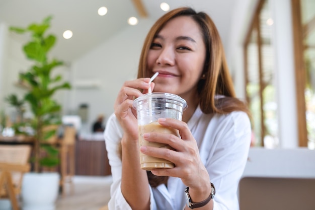 Immagine del ritratto di bella giovane donna asiatica che tiene e che beve caffè freddo nella caffetteria