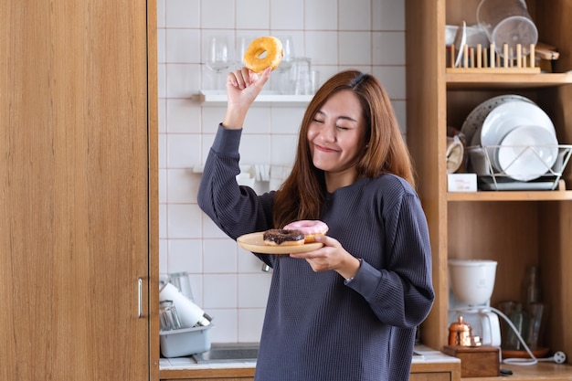 Immagine del ritratto di una bella giovane donna asiatica che tiene ciambelle e balla in cucina a casa