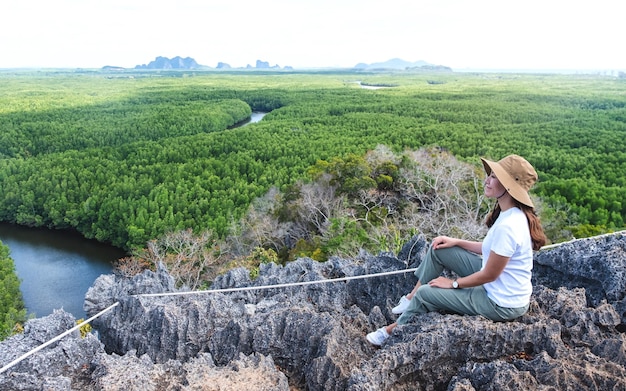 Immagine del ritratto di una giovane e bella donna asiatica seduta sulla cima della montagna mentre si viaggia per il punto di vista della foresta di mangrovie