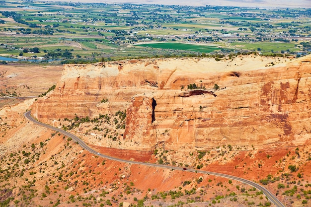 Immagine dell'avvolgimento della strada contro grandi montagne di roccia rossa con un deserto di terreni agricoli sullo sfondo