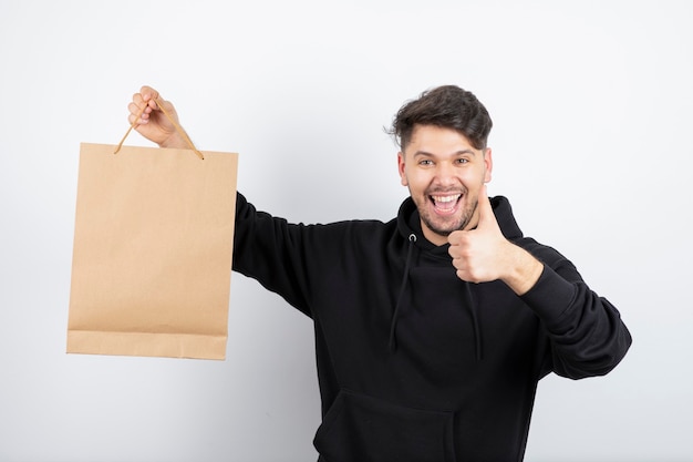 Immagine dell'uomo bello in felpa con cappuccio nera che tiene la borsa del mestiere che dà i pollici in su