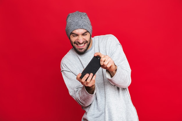Immagine dell'uomo positivo 30s che tiene smartphone e che gioca ai videogiochi, isolata