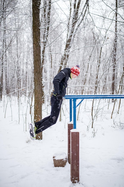 Immagine dell'uomo sportivo sulla barra orizzontale in inverno nei boschi