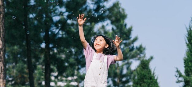 Immagine della bambina asiatica che gioca con le bolle di sapone al parco