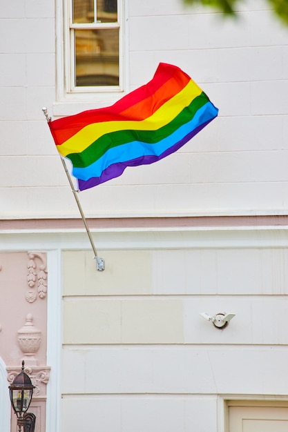 Immagine della bandiera dell'orgoglio arcobaleno stesa nel vento contro un edificio bianco con garage bianco