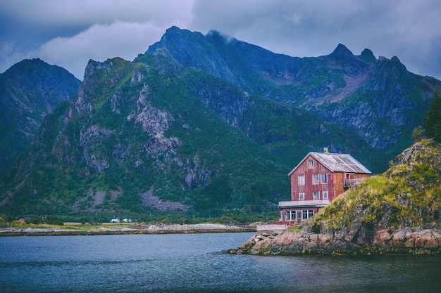 Immagine della casa rossa ai piedi degli alberi del cielo nuvoloso del mare delle colline in Norvegia