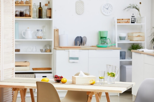 Immagine della cucina domestica con mobili bianchi e tavolo con bevande e frutta su di esso in casa