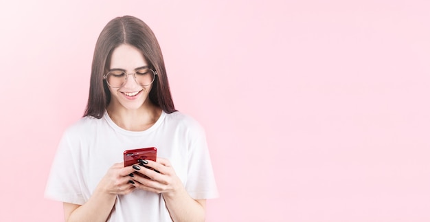 Immagine della donna americana felice che sorride e che utilizza il cellulare isolato sopra la parete rosa con copyspace