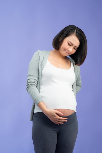 Immagine della donna incinta triste che posa isolata sopra la parete lilla